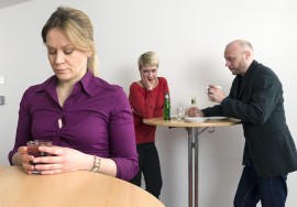 Frau mit gesenktem Blick wird von anderen Personen beobachtet