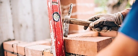 Helfer beim Bauarbeiten Ziegelsteine und Hand mit Hammer