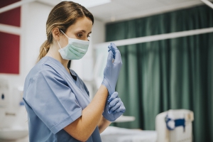 Krankenpflegerin mit OP-Maske zieht sich Gummihandschuhe an
