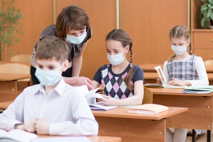 Lehrerin und Schüler*innen mit Mund-und Nasenschutz im Klassenraum