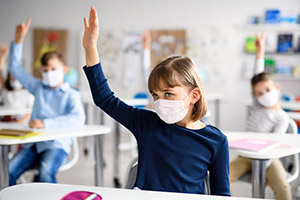 Schülerin mit Mund- und Nasenschutz meldet sich im Klassenraum