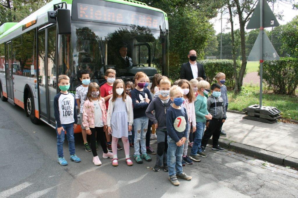 Kinder mit Mund- und Nasenschutz stehen vor Schulbus